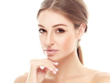 A woman with light brown hair is looking at the camera with her hand touching her chin. The background is white.